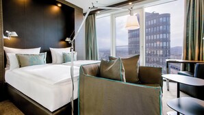 A modern hotel room with a large bed, a sofa, a desk, and a view of a cityscape. - Motel One Wien-Hauptbahnhof (Vienna)