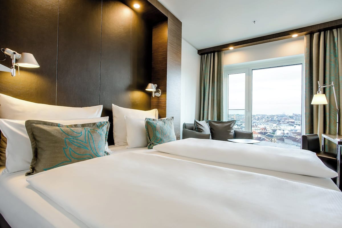 Habitación de hotel con una cama grande, dos mesitas de noche, un escritorio y una ventana con vistas a la ciudad.