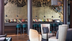 A bar area with a variety of liquor bottles, bar stools, and a seating area with cushioned chairs. - Motel One Wien-Hauptbahnhof (Vienna)