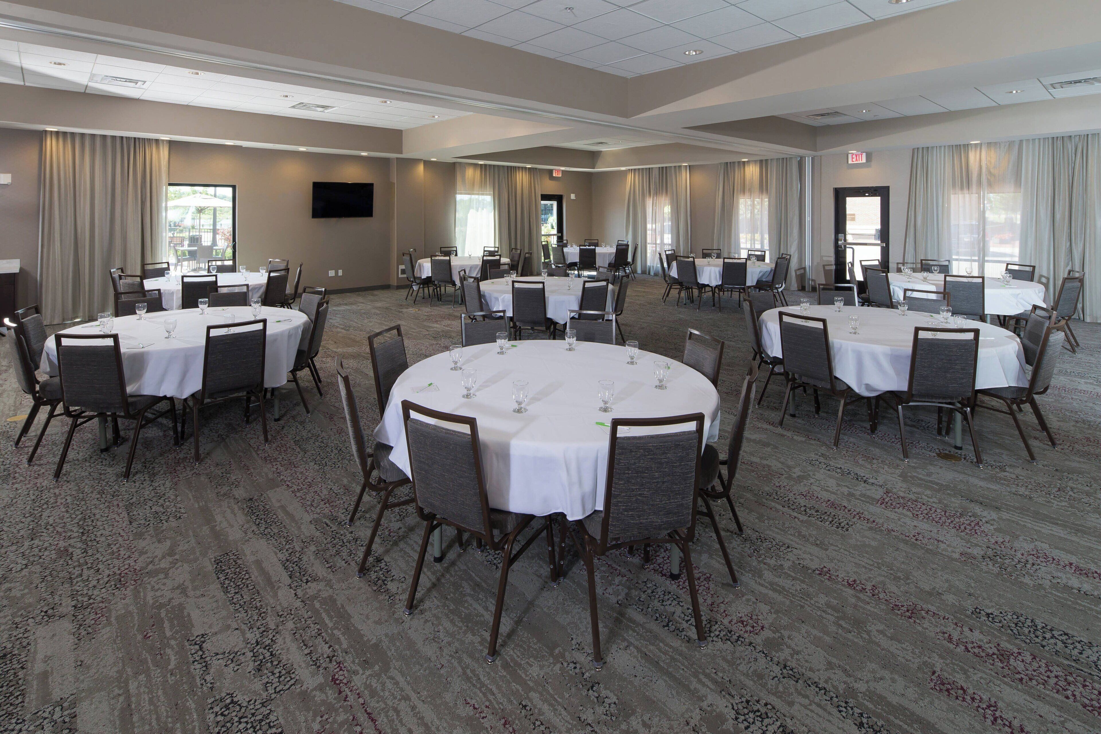 A large conference room with multiple round tables, each set with chairs and white tablecloths.