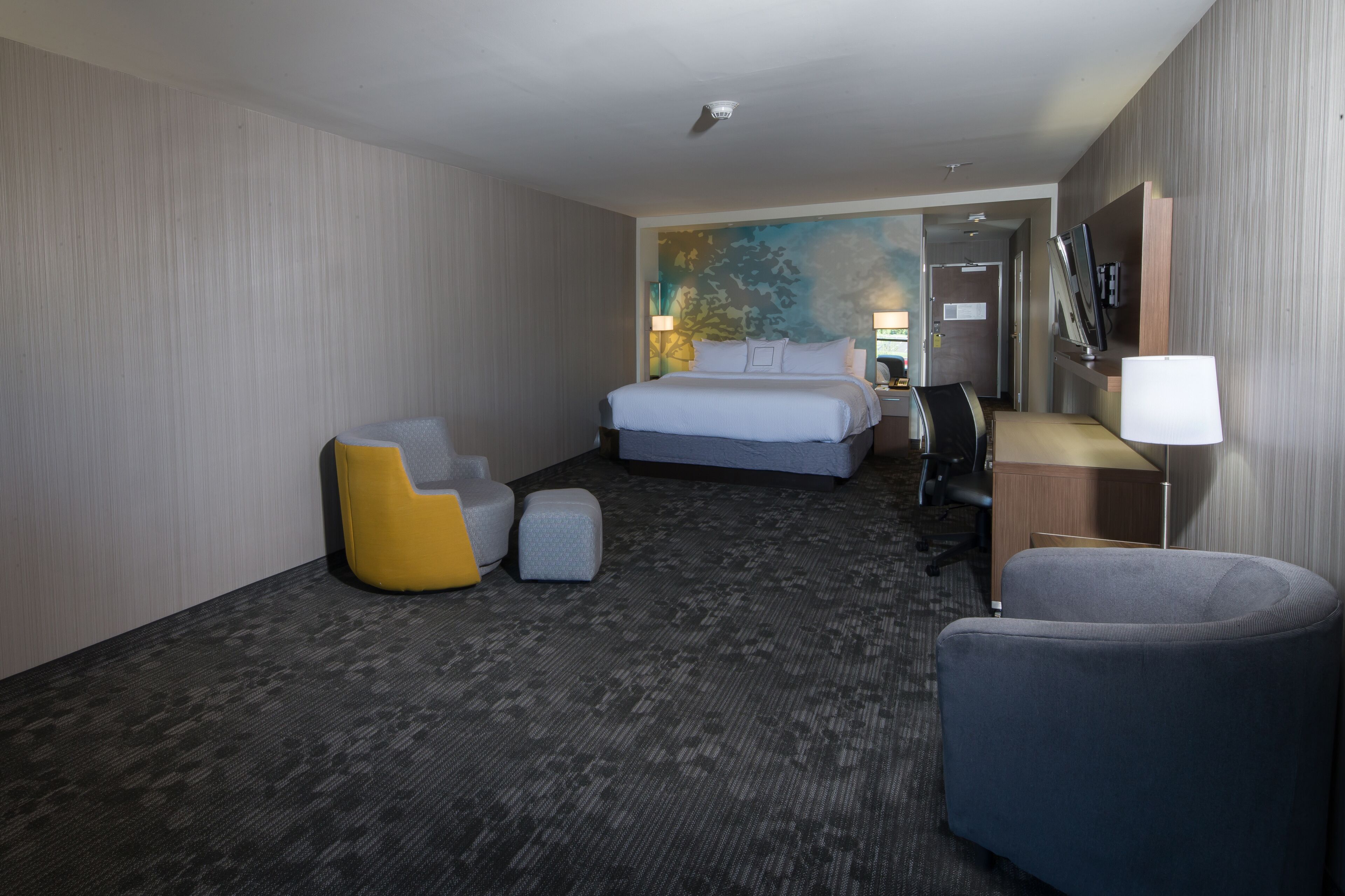 A hotel room with a large bed, a desk with a chair, a small sofa, and a lamp.
