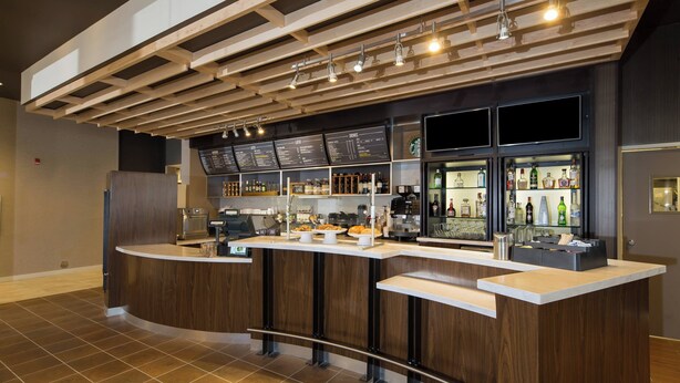 Zona de bar moderna con una barra curva, paneles de madera y una pizarra de menú.