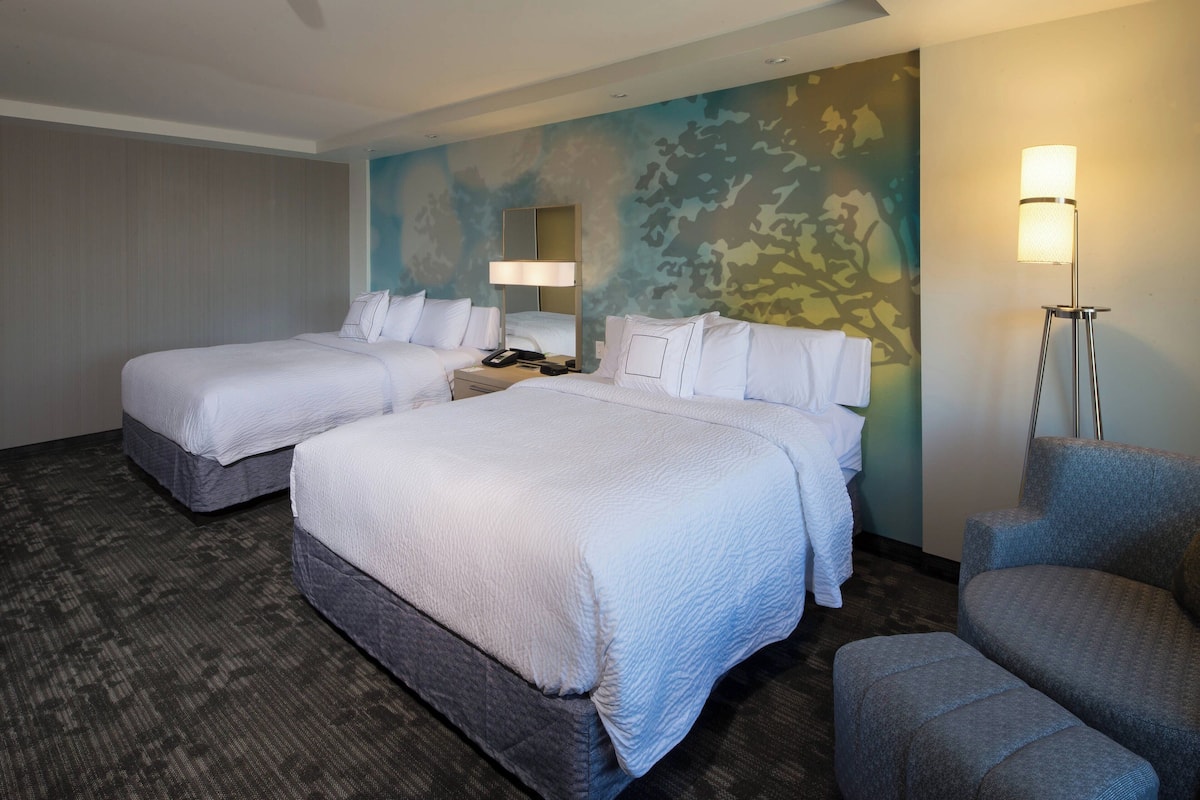 Ein Hotelzimmer mit zwei Betten, einem Schreibtisch, einem Stuhl und einer Stehlampe.