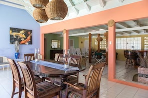 Uma sala de jantar com uma grande mesa de madeira, várias cadeiras e luminárias de vime penduradas.