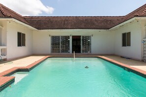 A swimming pool with a tiled deck, a tiled roof, and a door with metal bars. - Gemini Villa (Montego Bay)