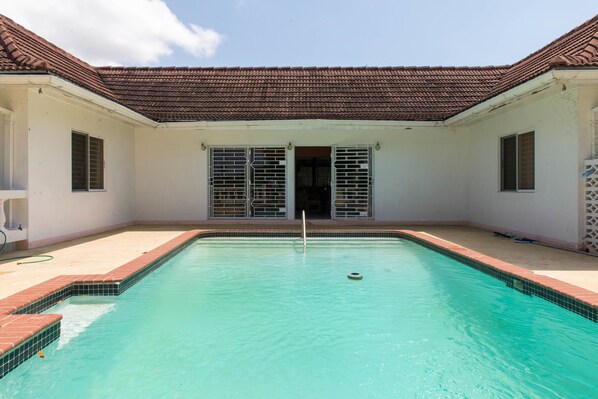 Une piscine dotée d’une terrasse carrelée, d’un toit recouvert de tuiles et d’une porte avec des barreaux en métal.