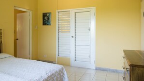 A bedroom with a bed, a wardrobe, and a painting on the wall. - Gemini Villa (Montego Bay)