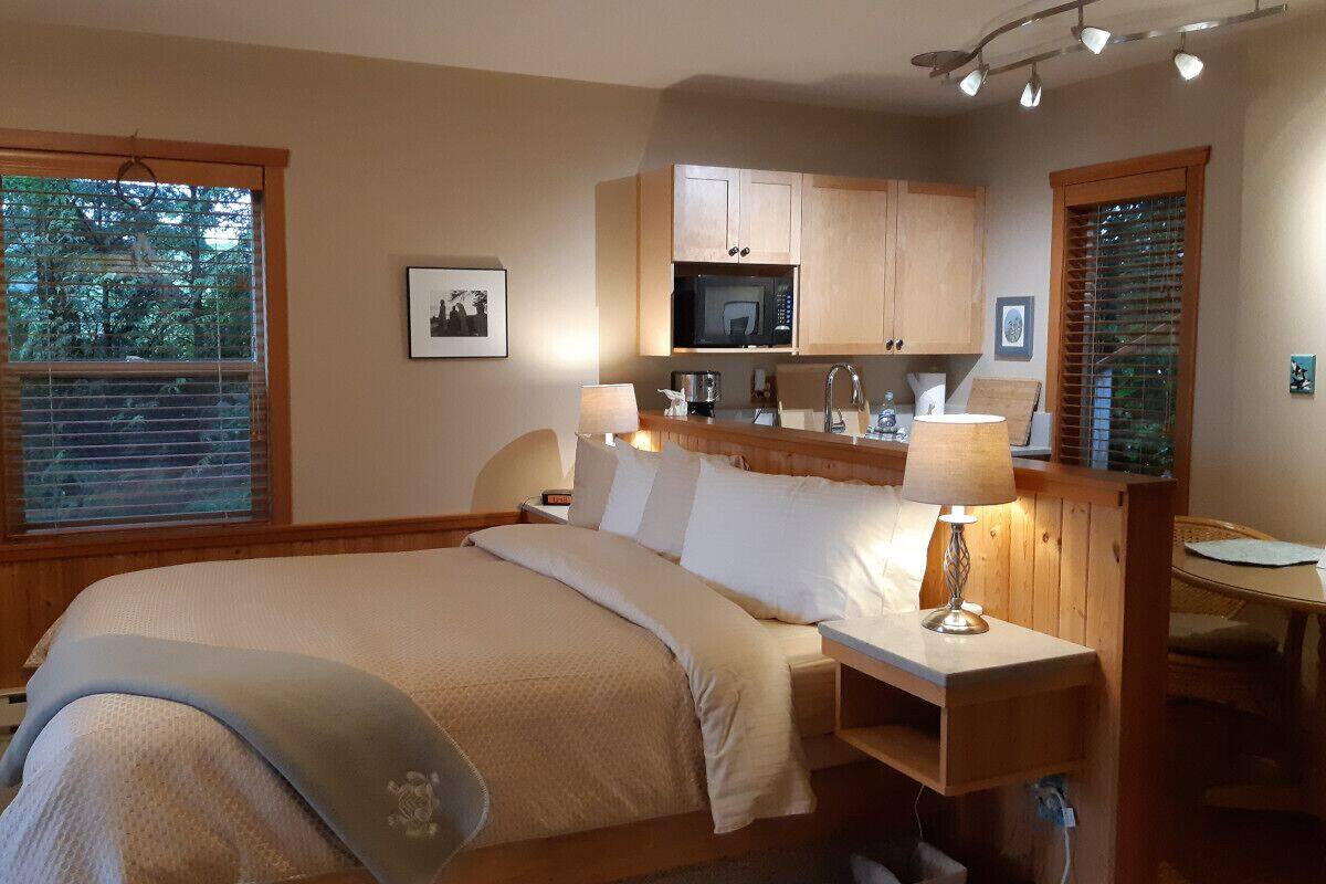 Un dormitorio con una cama, mesitas de noche, una lámpara, una mesita pequeña y una kitchenette con microondas.