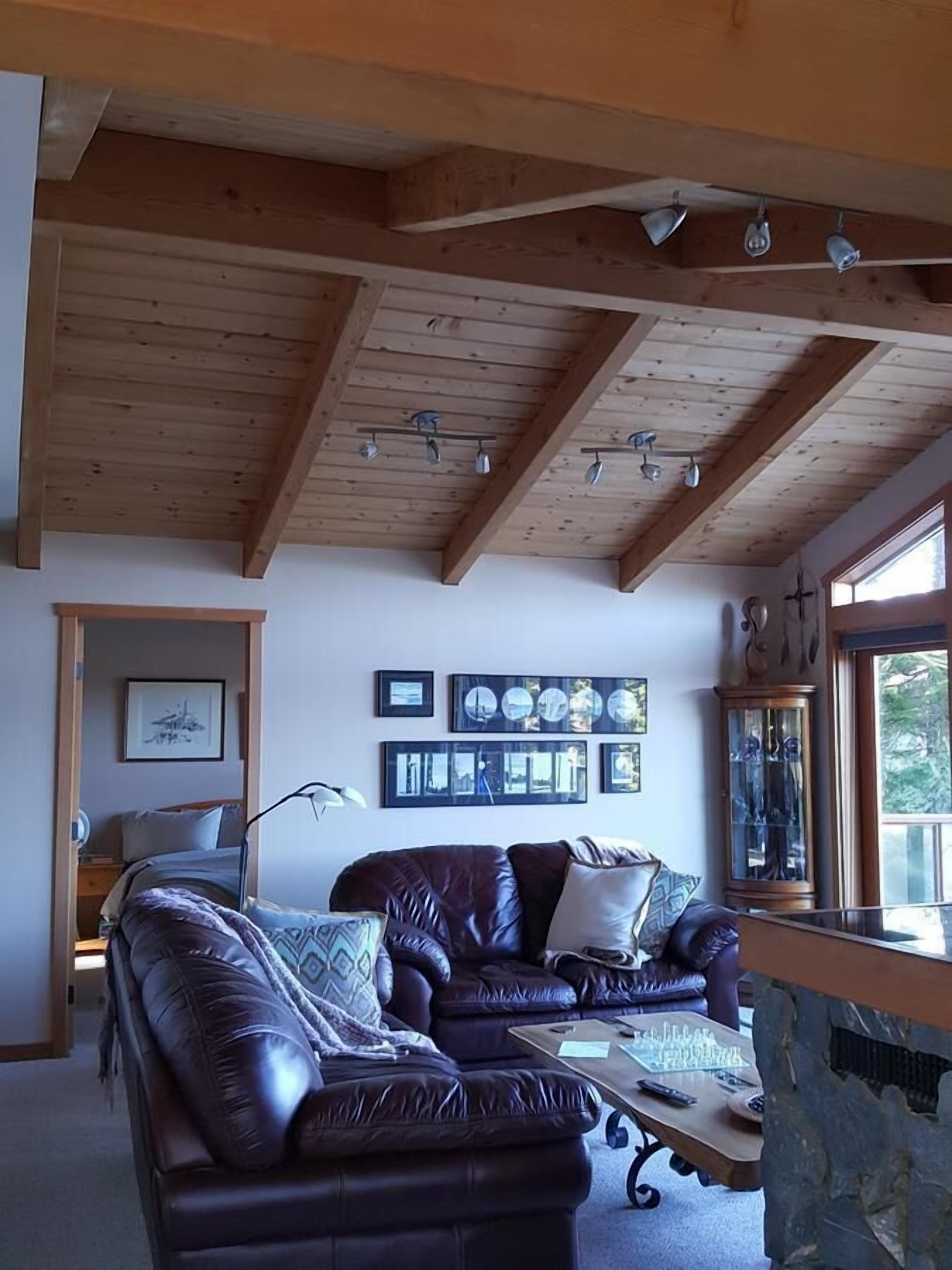 Un salon chaleureux avec un plafond en bois, un canapé en cuir, une table basse et un meuble avec des portes en verre.