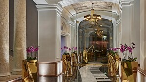 Un hall d’entrée luxueux, avec un sol en marbre, des éléments décoratifs dorés et des orchidées en pot.