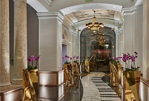 A luxurious hallway with marble floors, gold accents, and potted orchids.