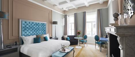 A hotel room with a large bed, a desk, a chair, and a fireplace.