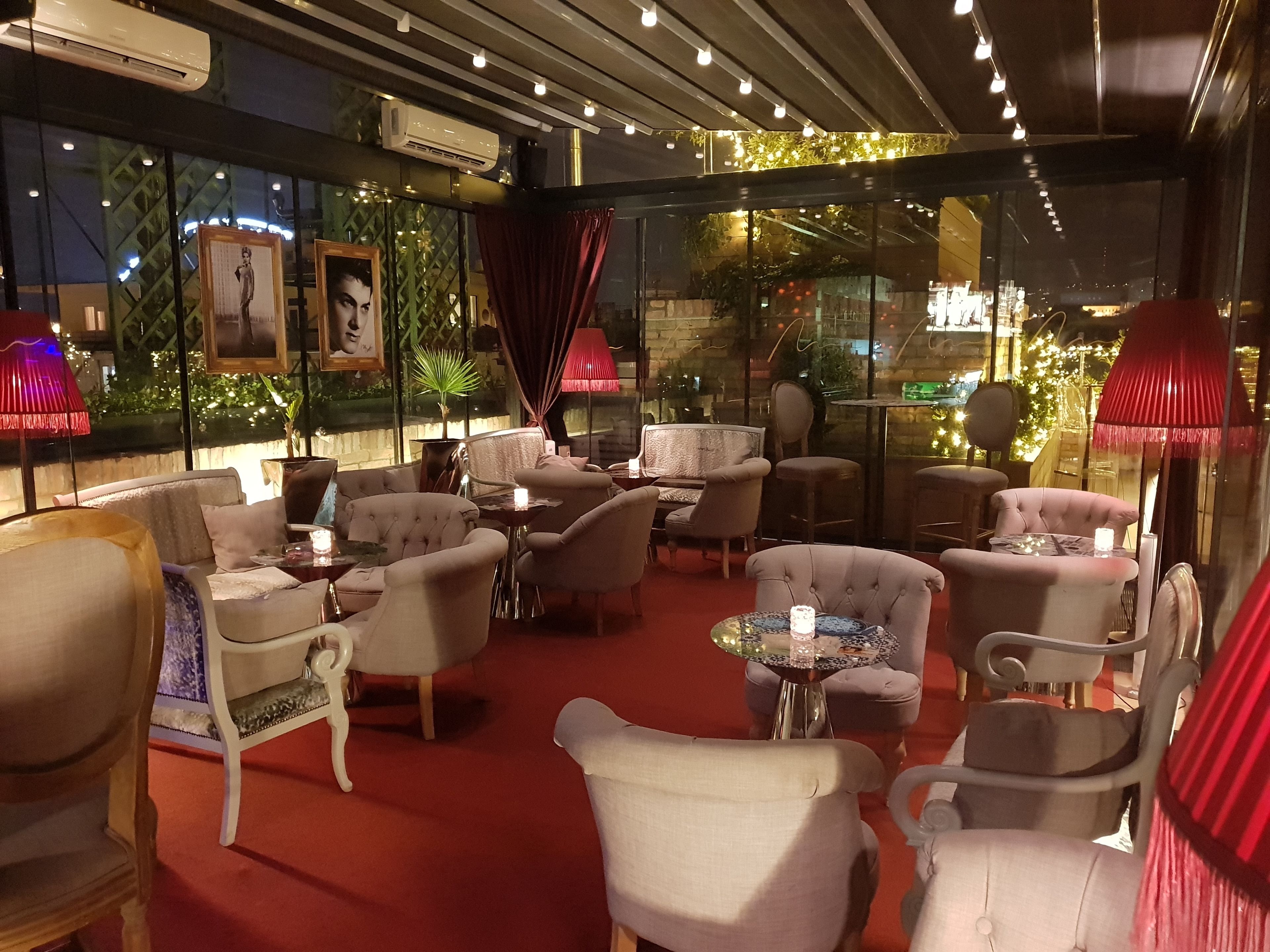 A cozy indoor seating area with plush chairs and tables, a red carpet, and decorative lighting.