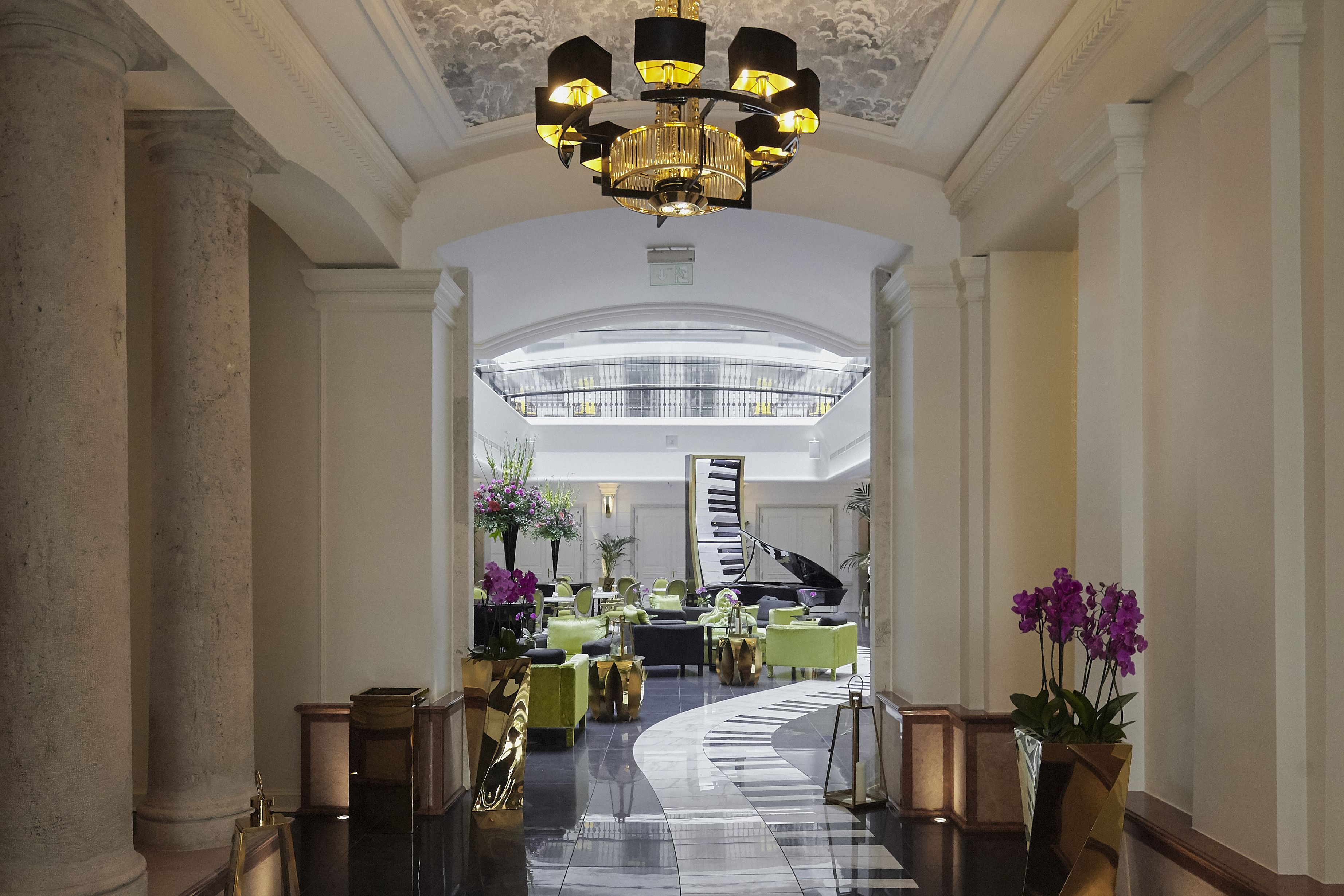 A grand lobby with a curved staircase, a grand piano, and a chandelier.