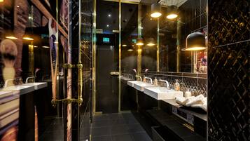 Un baño moderno con varios lavamanos, mampara de vidrio e iluminación decorativa.
