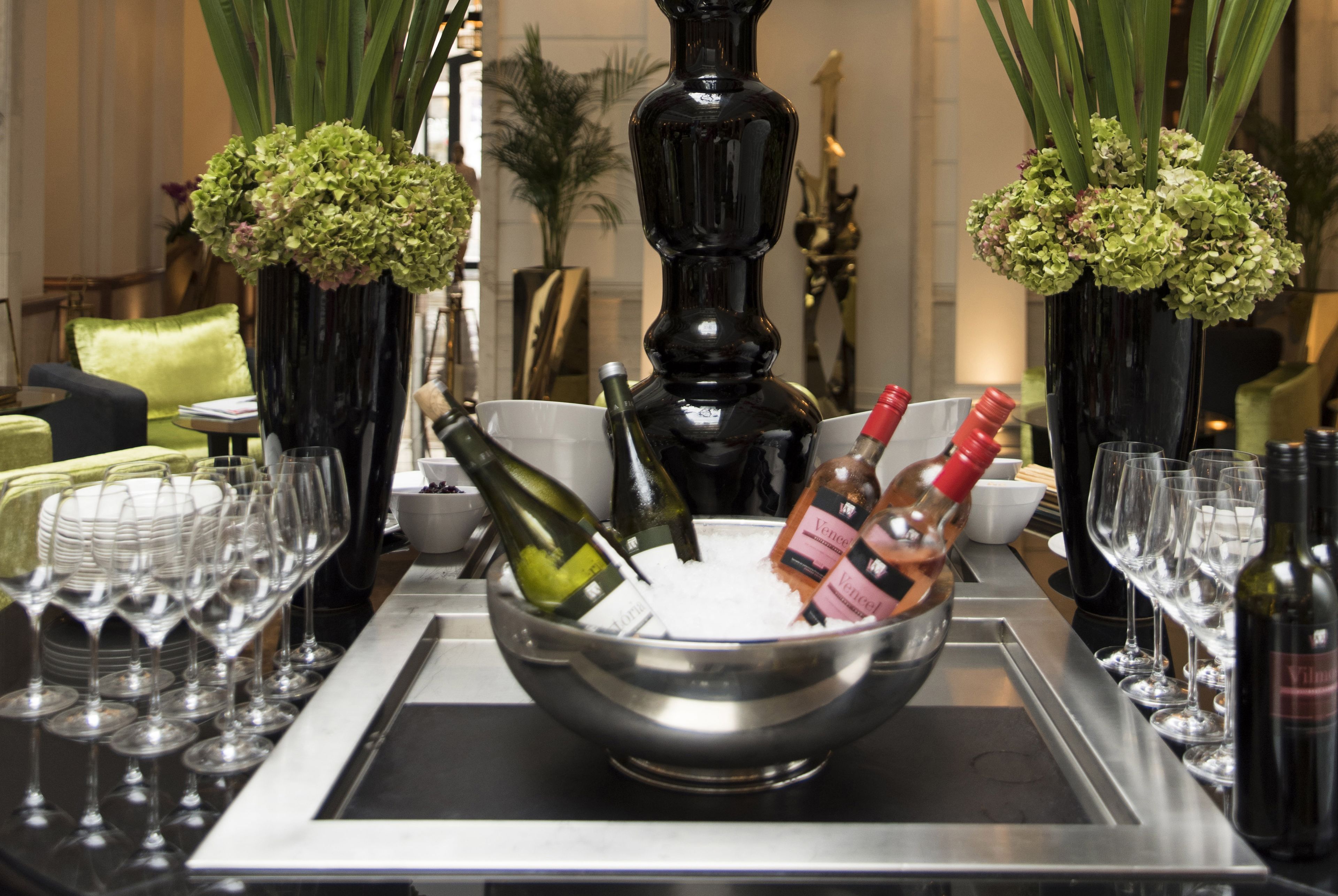 A bar area with a metal tray holding wine bottles and glasses, surrounded by vases with green flowers.