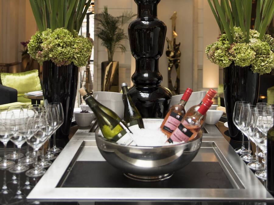 A bar area with a metal tray holding wine bottles and glasses, surrounded by vases with green flowers.