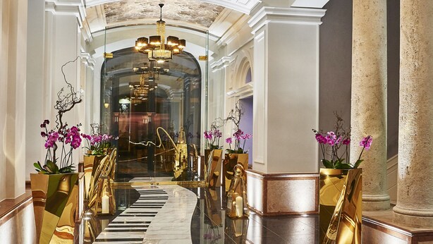 A grand hallway with a reflective marble floor, ornate columns, and a central chandelier. - Aria Hotel Budapest by Library Hotel Collection (Budapest)
