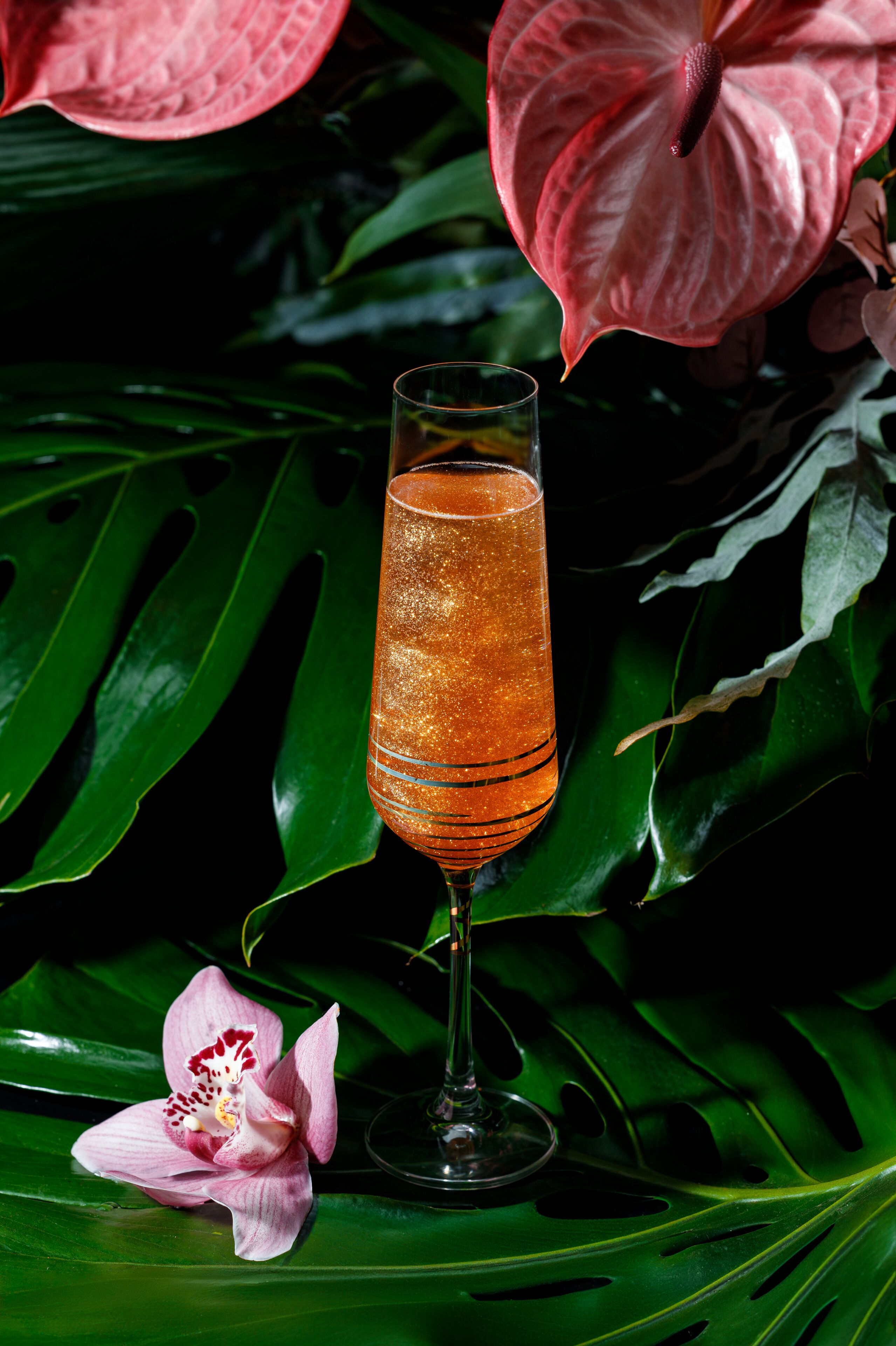 Ein Glas orangefarbenes Getränk mit einem Strohhalm, umgeben von grünen Blättern und einer rosa Blüte.