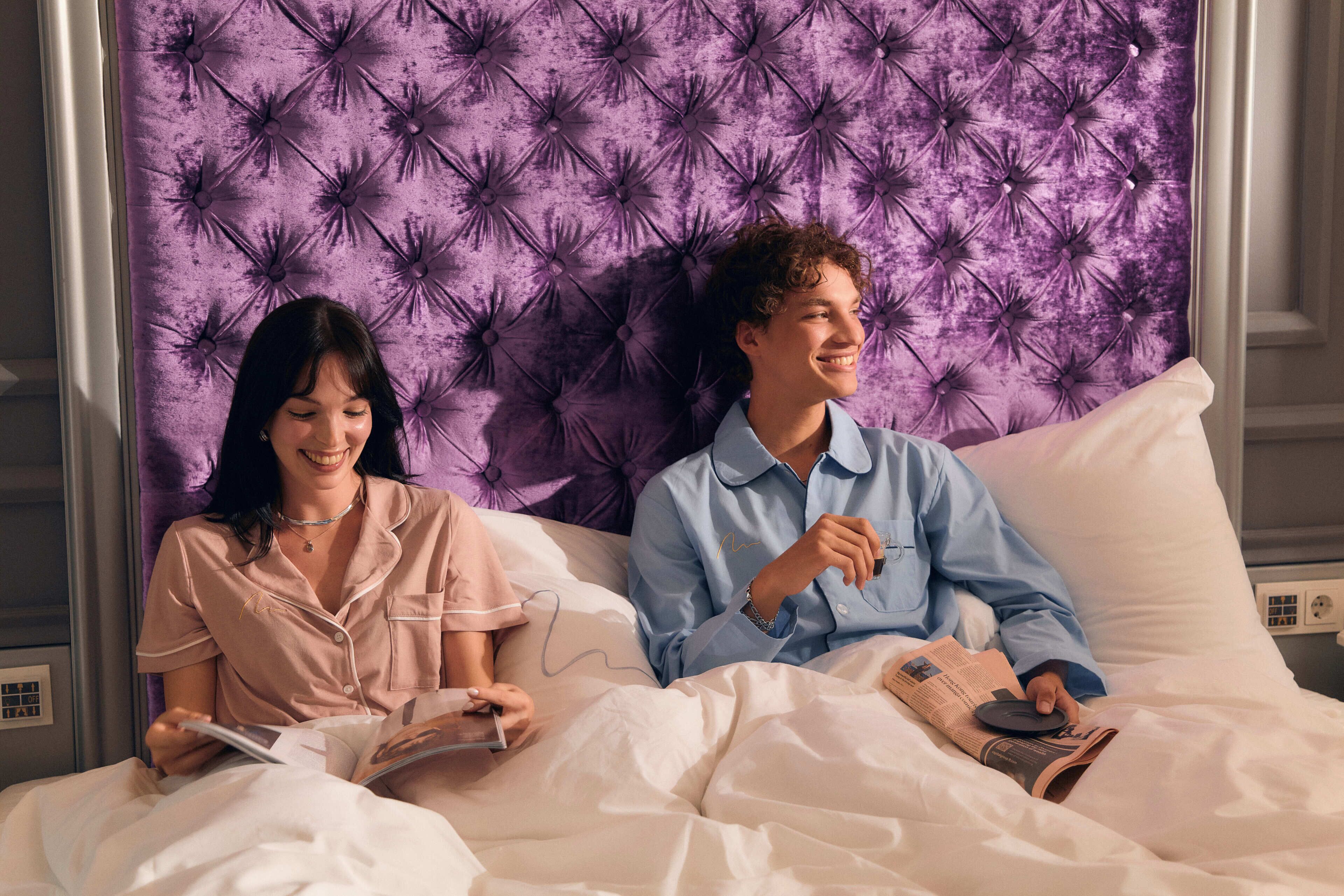 Een koppel zit op een bed met een gestoffeerd hoofdbord, terwijl ze een tijdschrift lezen.
