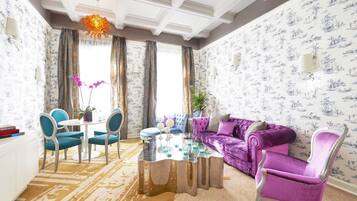 A living room with a purple sofa, blue chairs, a glass coffee table, and patterned wallpaper.