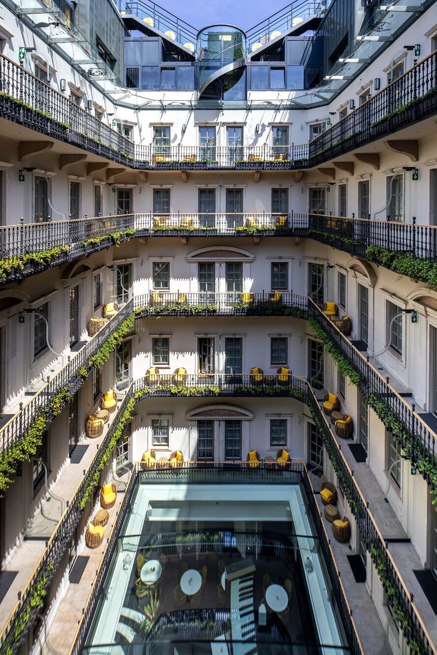Un edificio de varios pisos con balcones, mobiliario exterior y un atrio central con mesas y sillas.