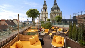 Une terrasse sur le toit, meublée de mobilier en osier, avec un magazine à portée de main et une vue sur des bâtiments historiques.