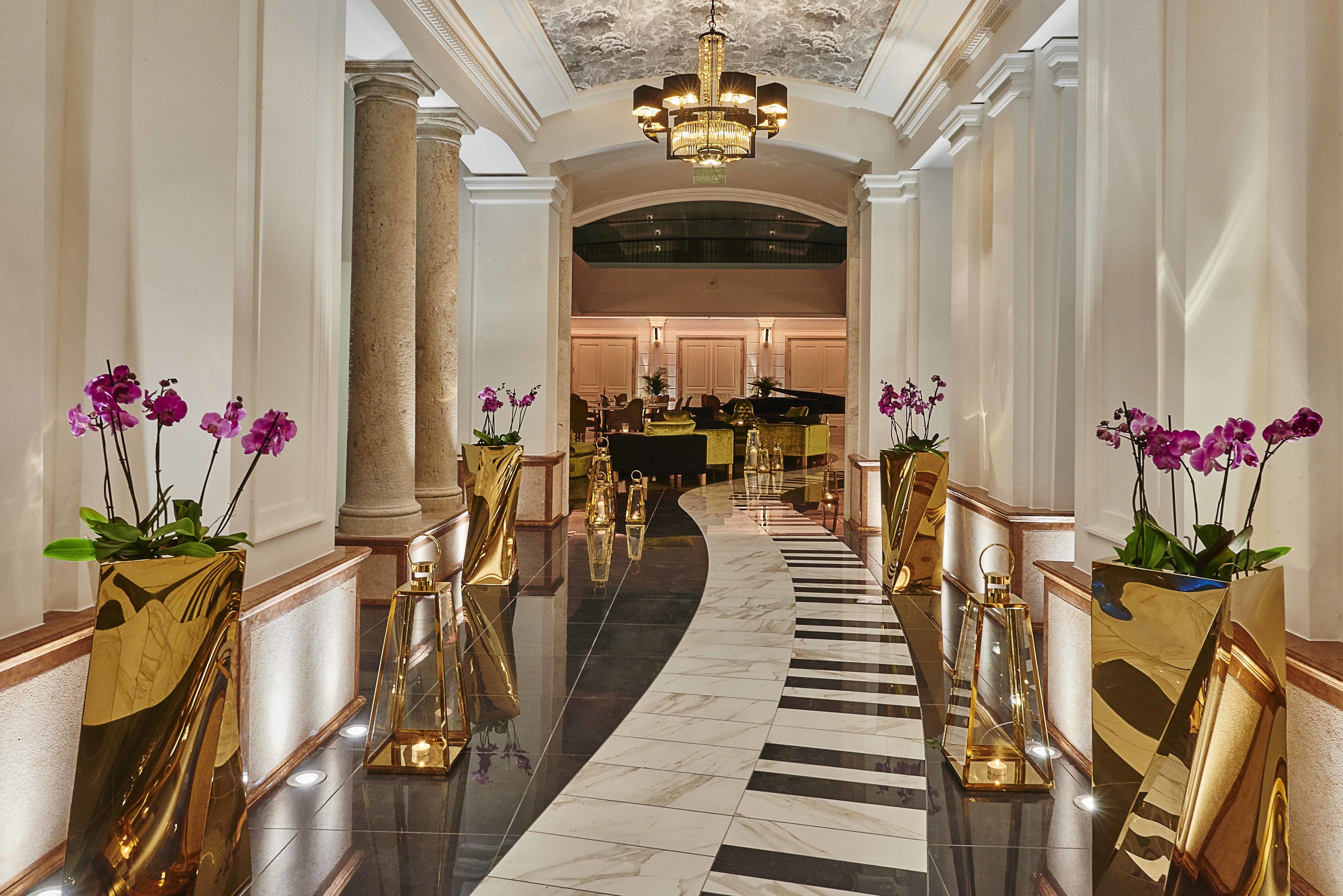 A grand hallway with marble flooring, gold accents, and purple orchids.
