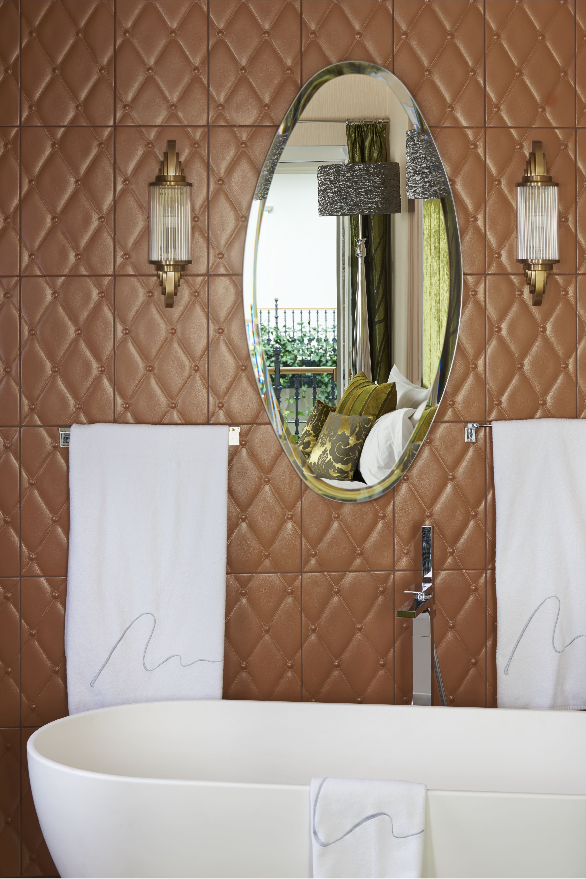 A bathroom with a large oval mirror, two wall-mounted light fixtures, and a white bathtub.