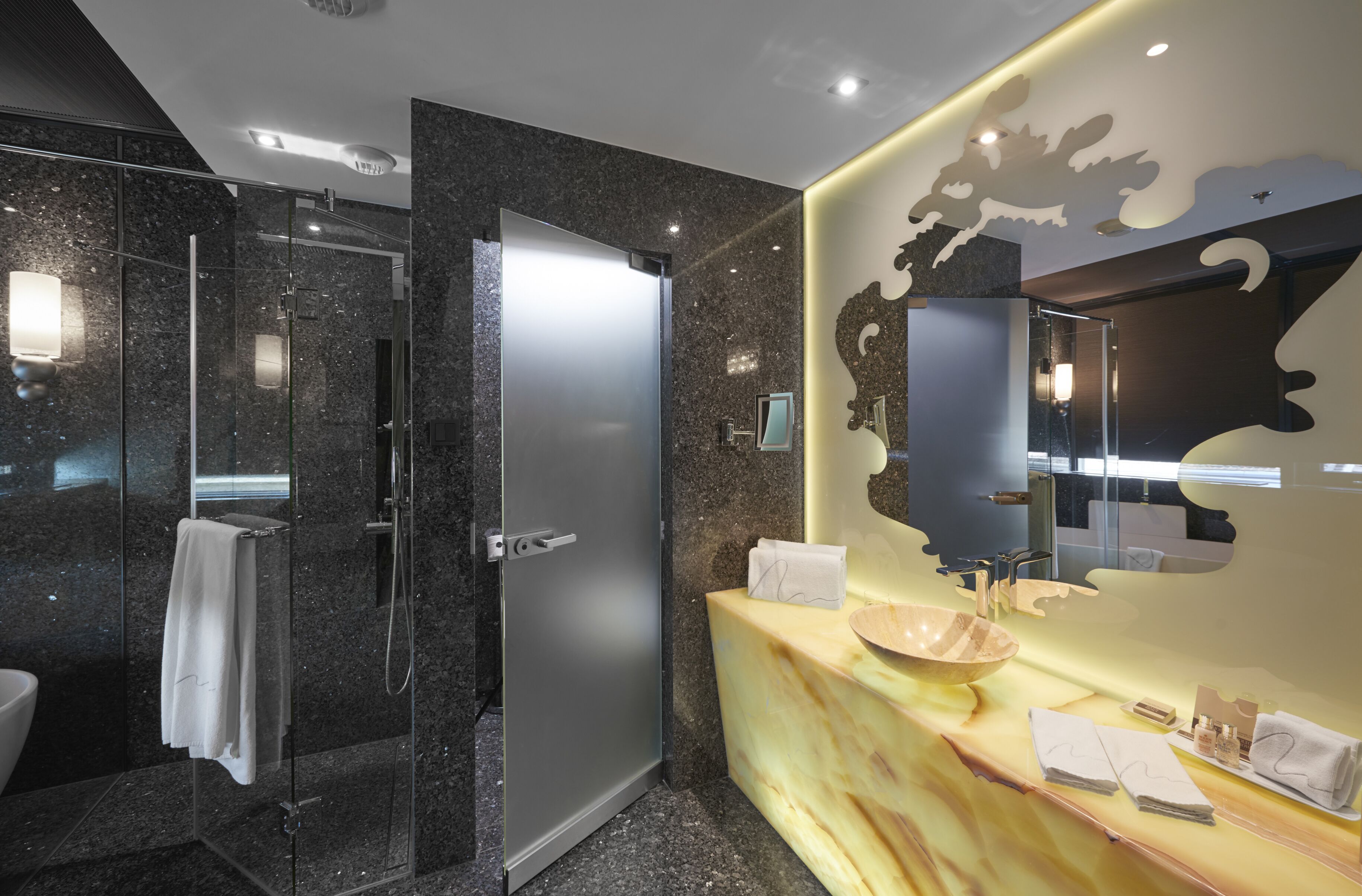 A modern bathroom with a glass-enclosed shower, a marble vanity with a large mirror, and a towel rack.