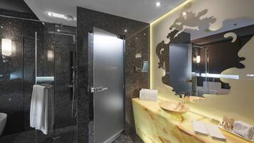 A modern bathroom with a glass-enclosed shower, a marble vanity with a large mirror, and a towel rack.