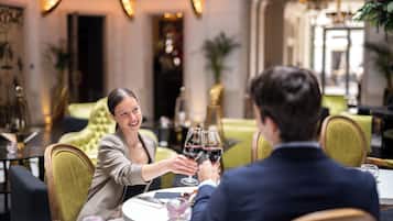 A couple toasting at a round table in a restaurant with a classic interior, including a green upholstered sofa and a chandelier.
