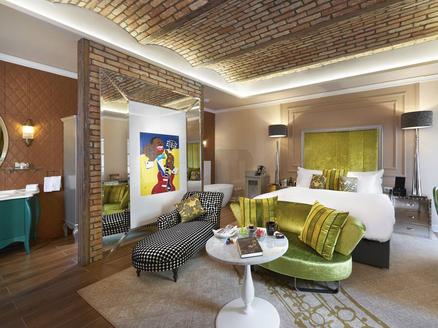 Habitación de hotel con una cama grande, un sofá, una mesa de comedor y un baño con espejo y lavamanos.