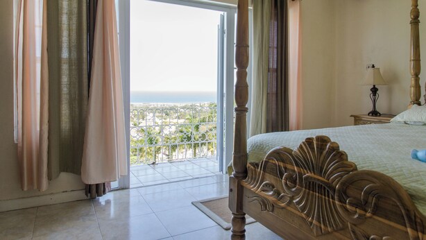 A bedroom with a large bed, a balcony with a view, and a ceiling fan.