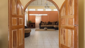 An open wooden door leading to a living room with a sectional sofa, a rug, and a ceiling fan.