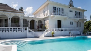 A two-story house with a swimming pool, white exterior, and a balcony.