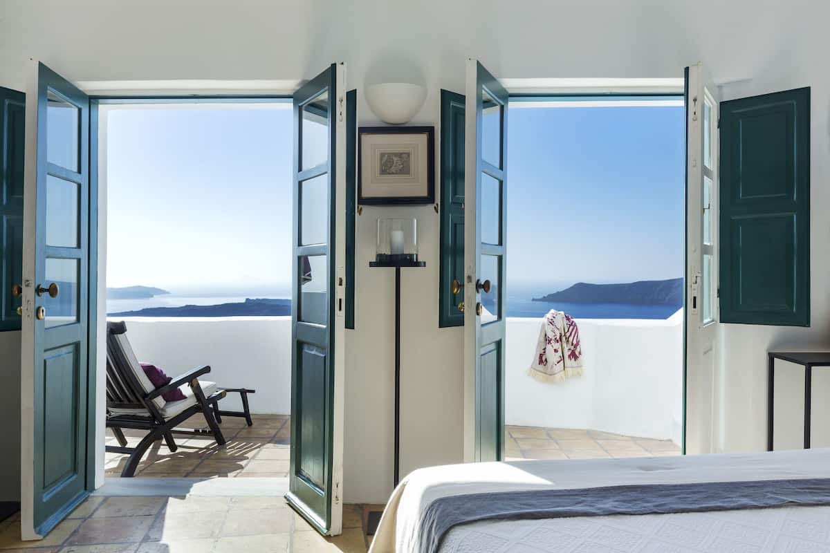 A room with an open door leading to a balcony with a view of the sea.