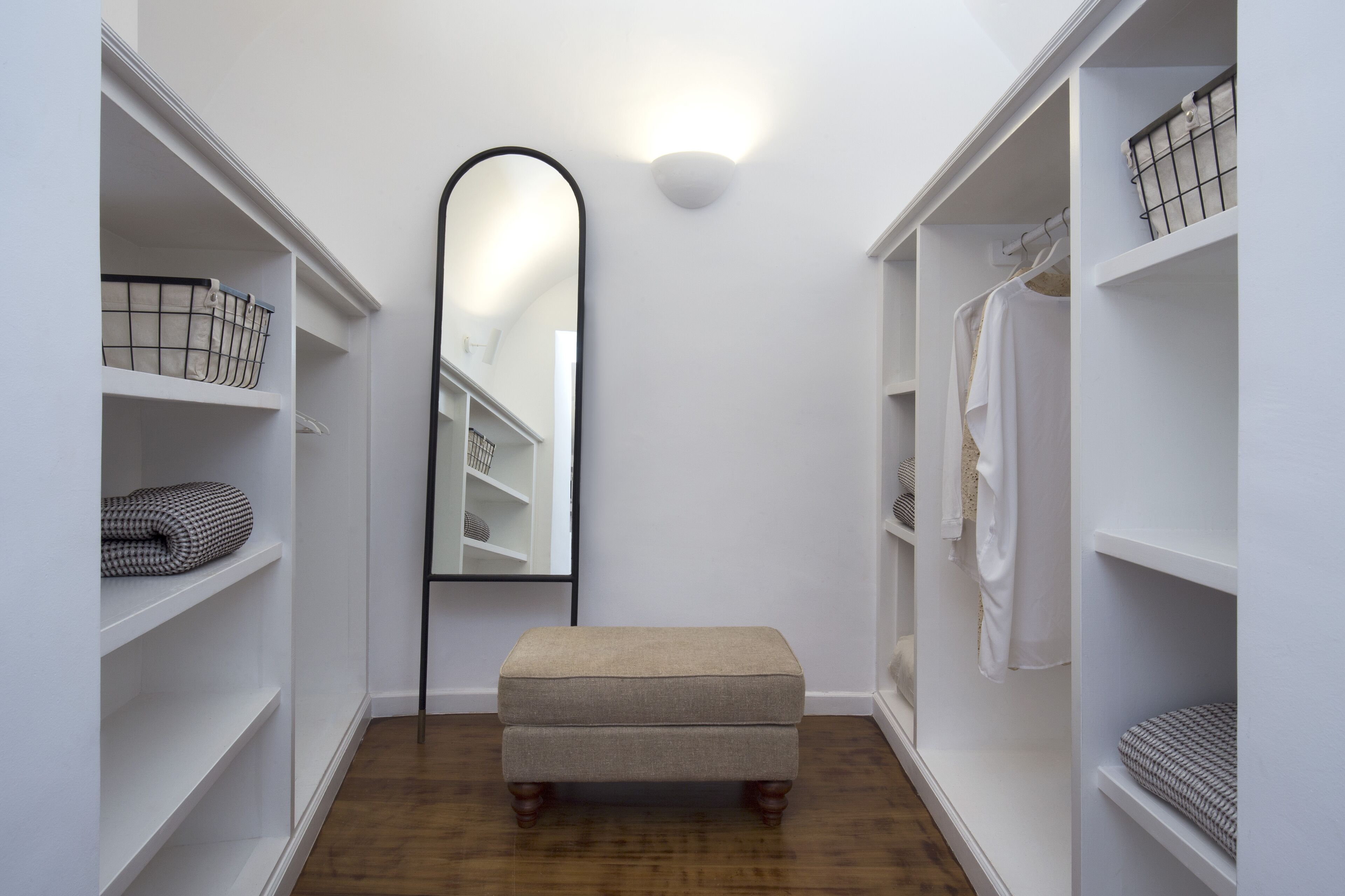A narrow hallway with white shelving units, a mirror, and a bench.