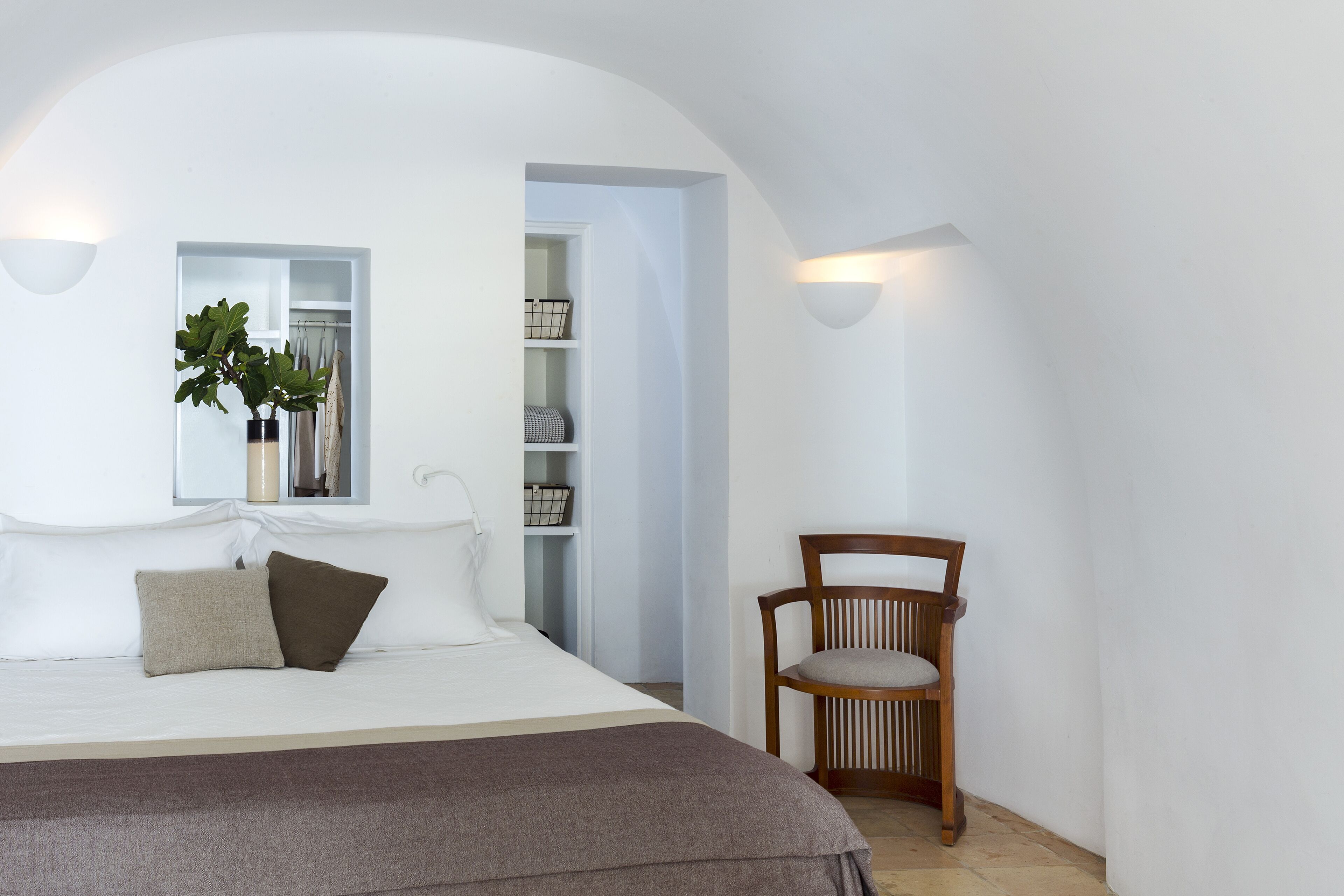 Quarto com cama, cadeira, mesa de cabeceira e prateleira com objetos.