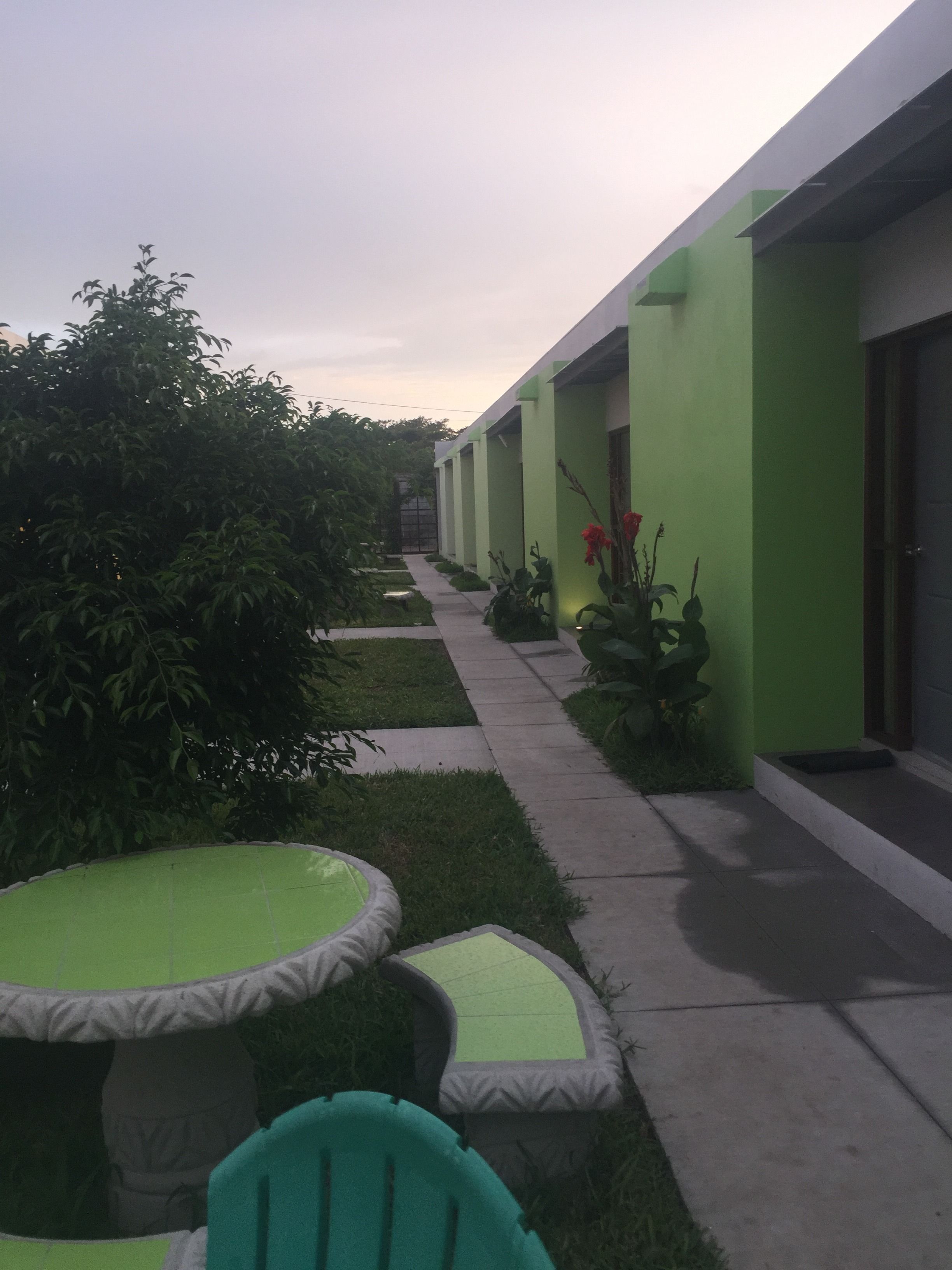 A pathway leading to a building with green walls and a covered outdoor seating area with a table and chairs.