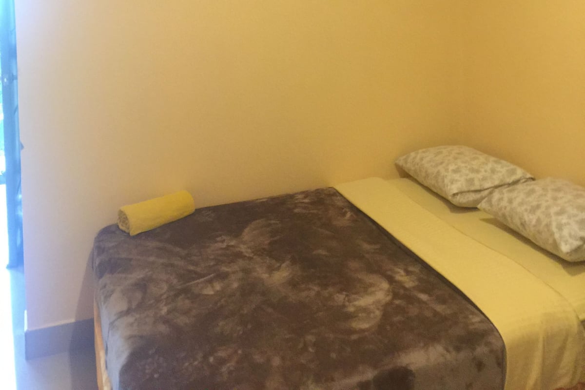 Una habitación con cama, almohada, manta y aire acondicionado en la pared.