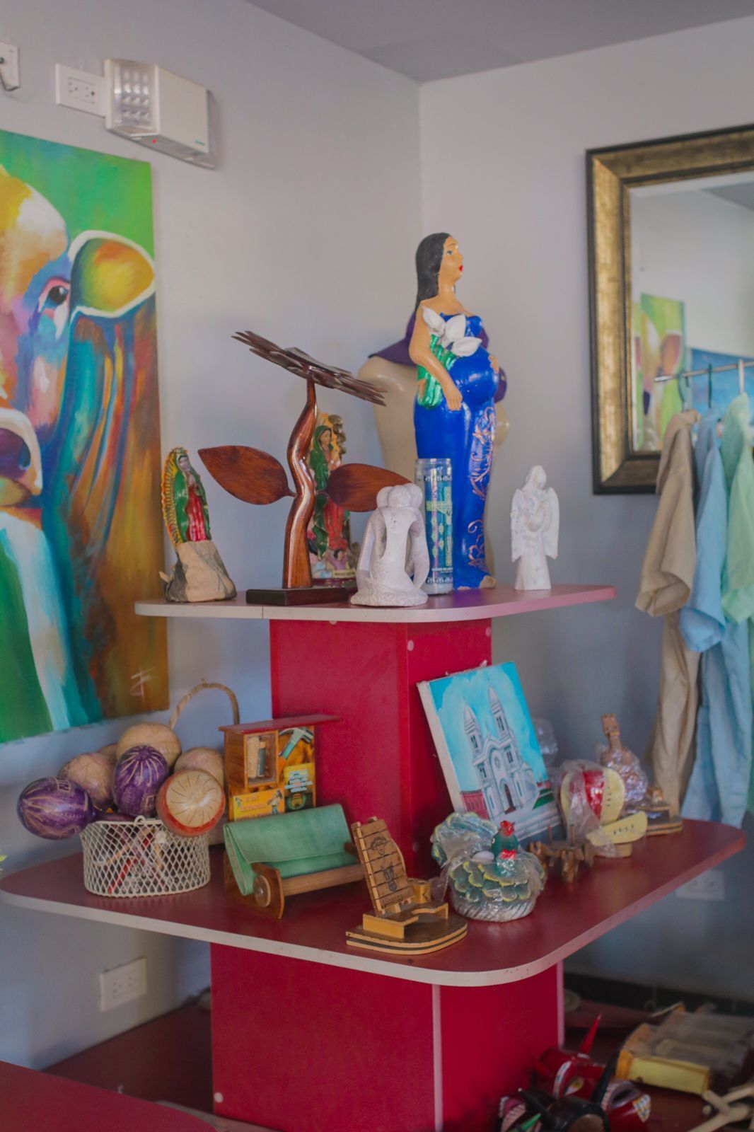 A room with a red and white shelf displaying various decorative items, including a mannequin, figurines, and a painting.