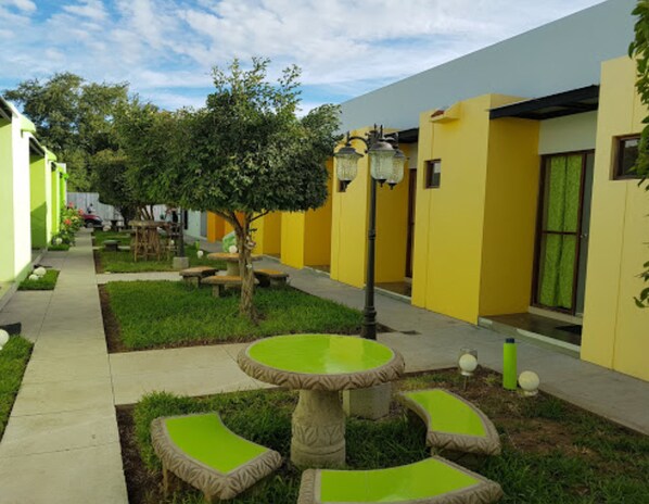 Un patio con una mesa redonda central rodeada de asientos verdes y acolchados, un árbol y un farol.