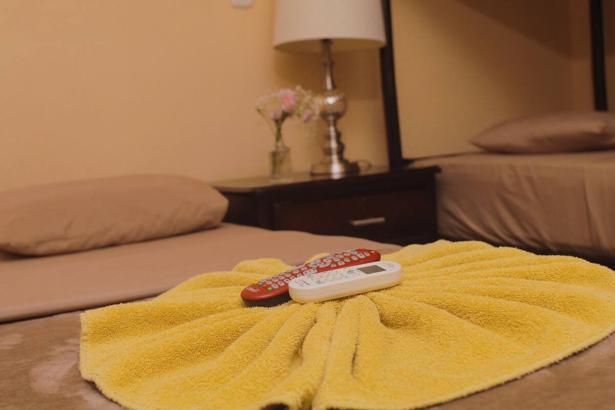 Una cama con una toalla amarilla y dos controles remotos.