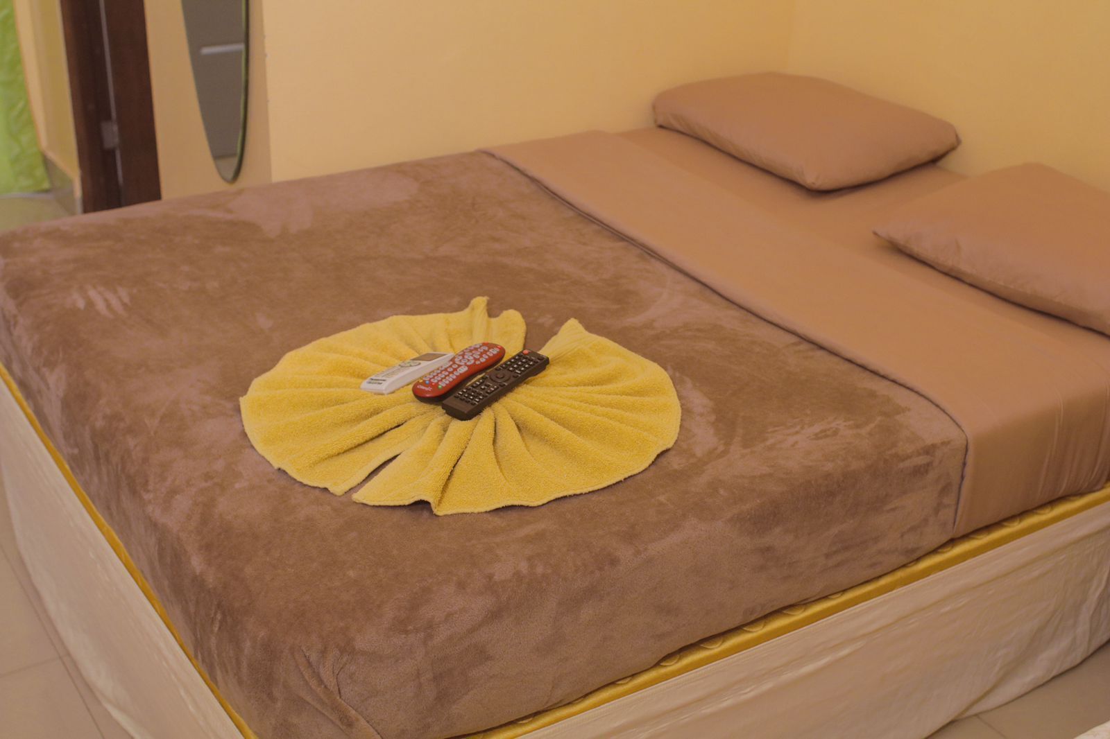 Una cama con una cubierta marrón, una toalla amarilla y dos controles remotos.