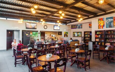A spacious restaurant with high ceilings, hanging pendant lights, and wooden tables and chairs.