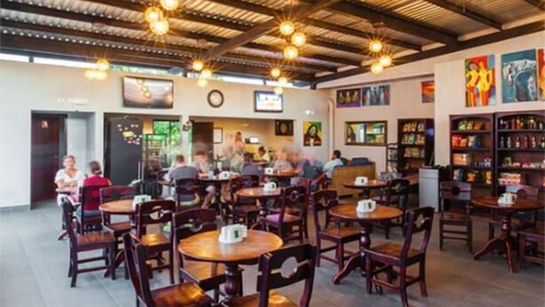 Un restaurante espacioso con techos altos, lámparas colgantes y mesas y sillas de madera.