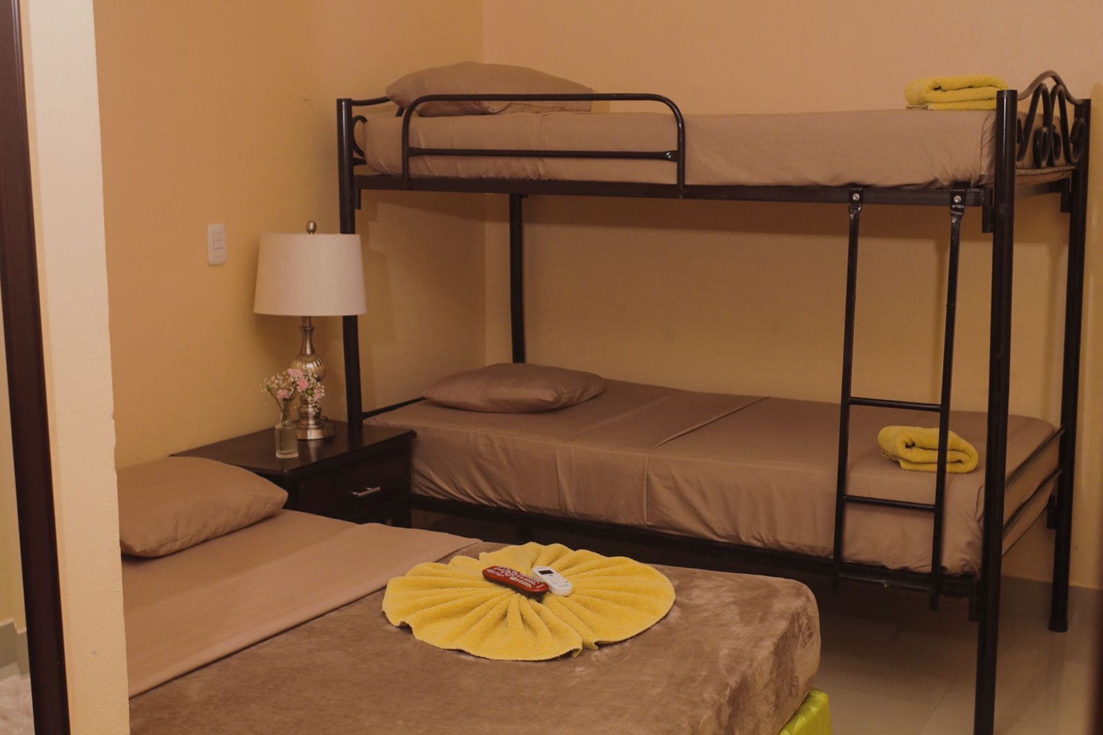 Habitación con literas, una lámpara y una mesita con un jarrón de flores.