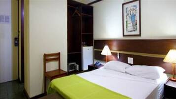 A hotel room with a bed, a nightstand, a lamp, a chair, a wardrobe, and a painting on the wall.
