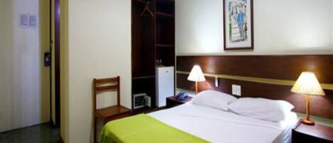 A hotel room with a bed, a nightstand, a lamp, a chair, a wardrobe, and a painting on the wall.